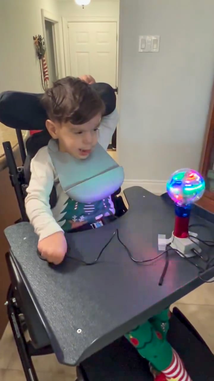 Sandro, in a wheelchair, playing a switch-adapted toy on his lap tray.