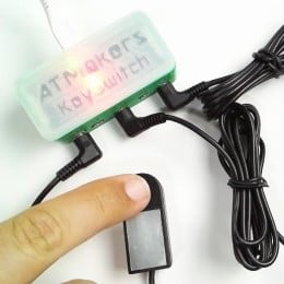 Picture of an ATMaker Keyswitch with several assistive switches plugged in. One switch is being pressed by a finger.