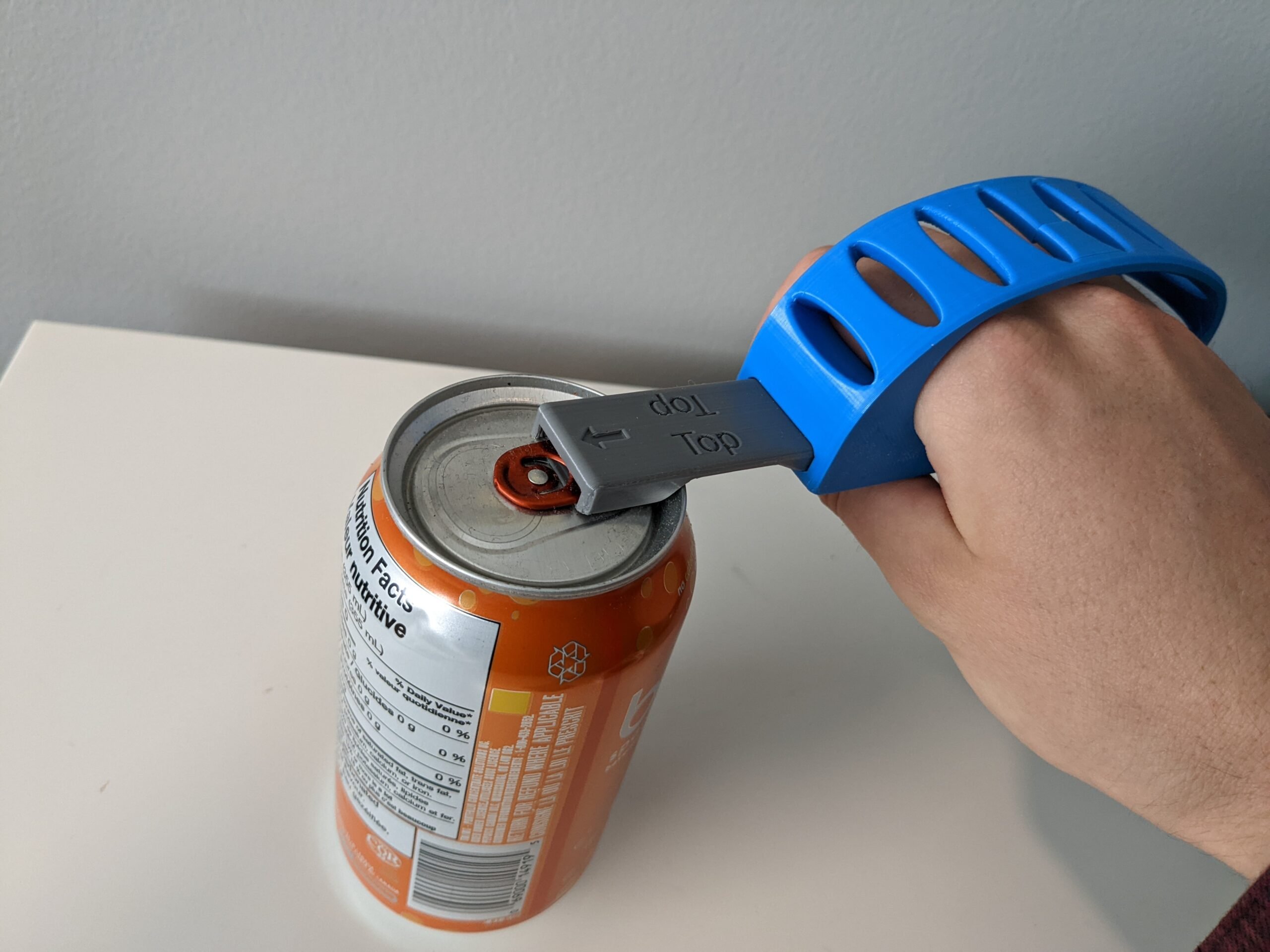 A hand looped through a 3d printed can opener to open a soda can.