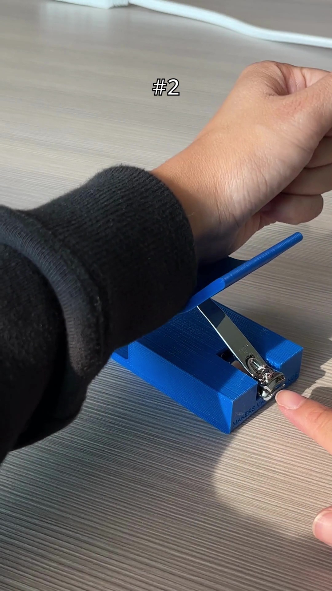 An arm pressing down on a blue 3d printed nail clipper holder.