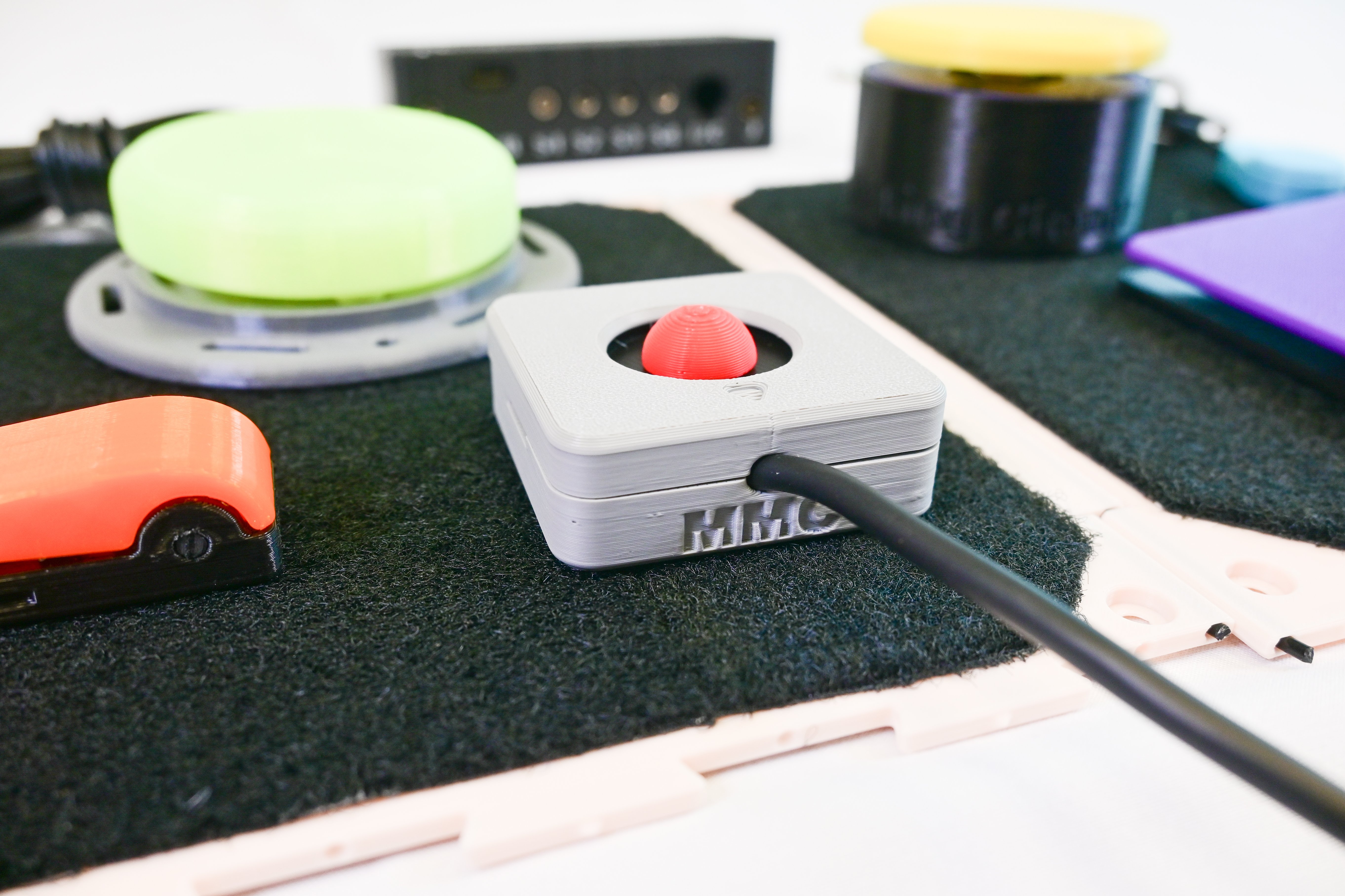 Close up photo of the Aspen joystick in focus on a gaming tray with other assistive tech in the background.