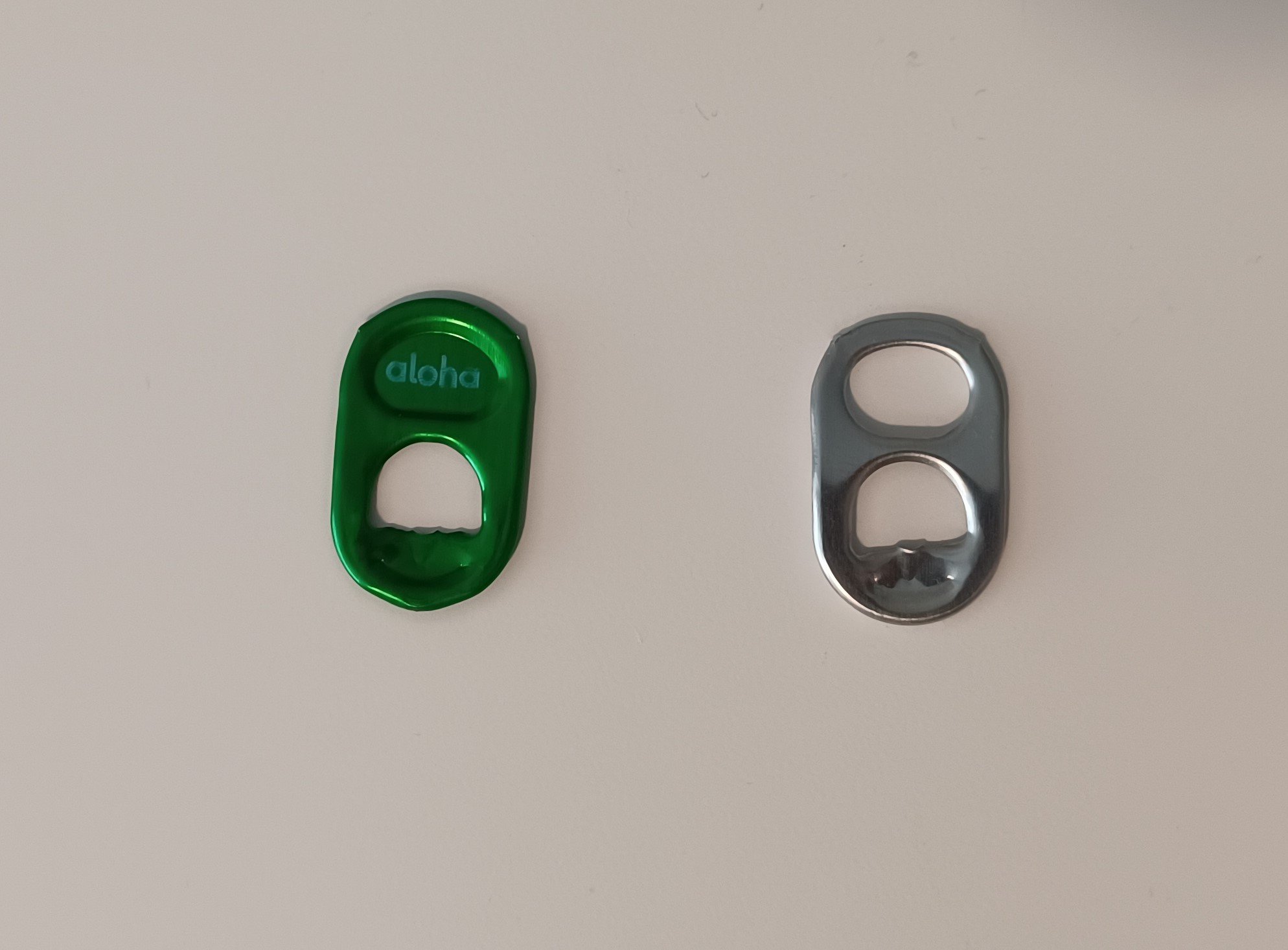 Two beverage can pull-tabs, left side pull-tab with a logo instead of a hole in the top. Right side has the generic hole in the top of the pull-tab.