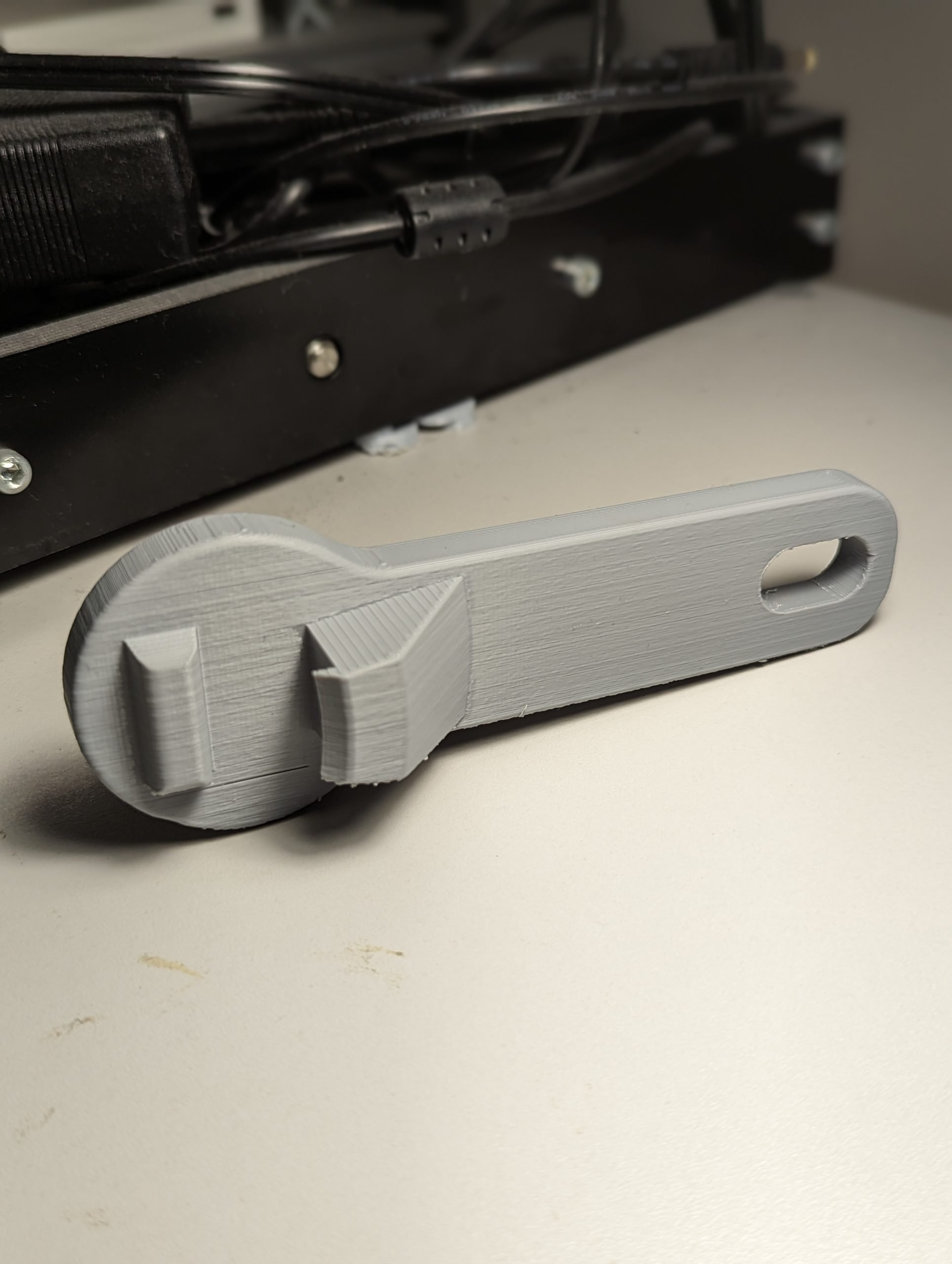 A grey 3d printed jar lid opener on a white table.