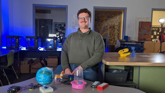 A man smiling at the camera with various 3d printed assistive technology in front of him