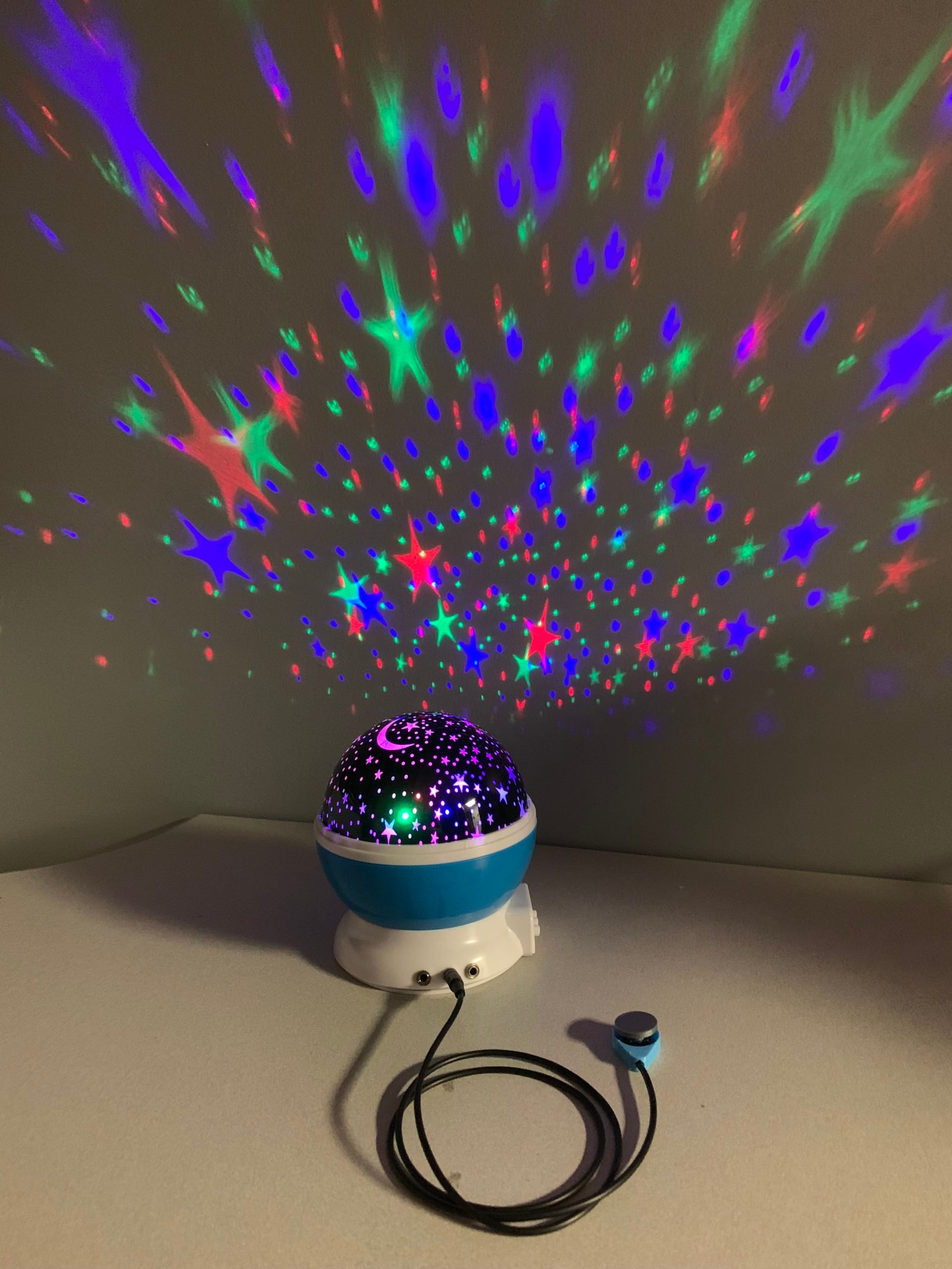 A switch adapted star light projector with a 3d printed assistive switch plugged in. The toy is projecting green, blue, and red stars on the wall.