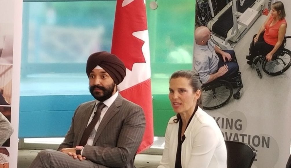 Two individuals photographed in front of a Canadian flag and banner at a Government of Canada funding panel.