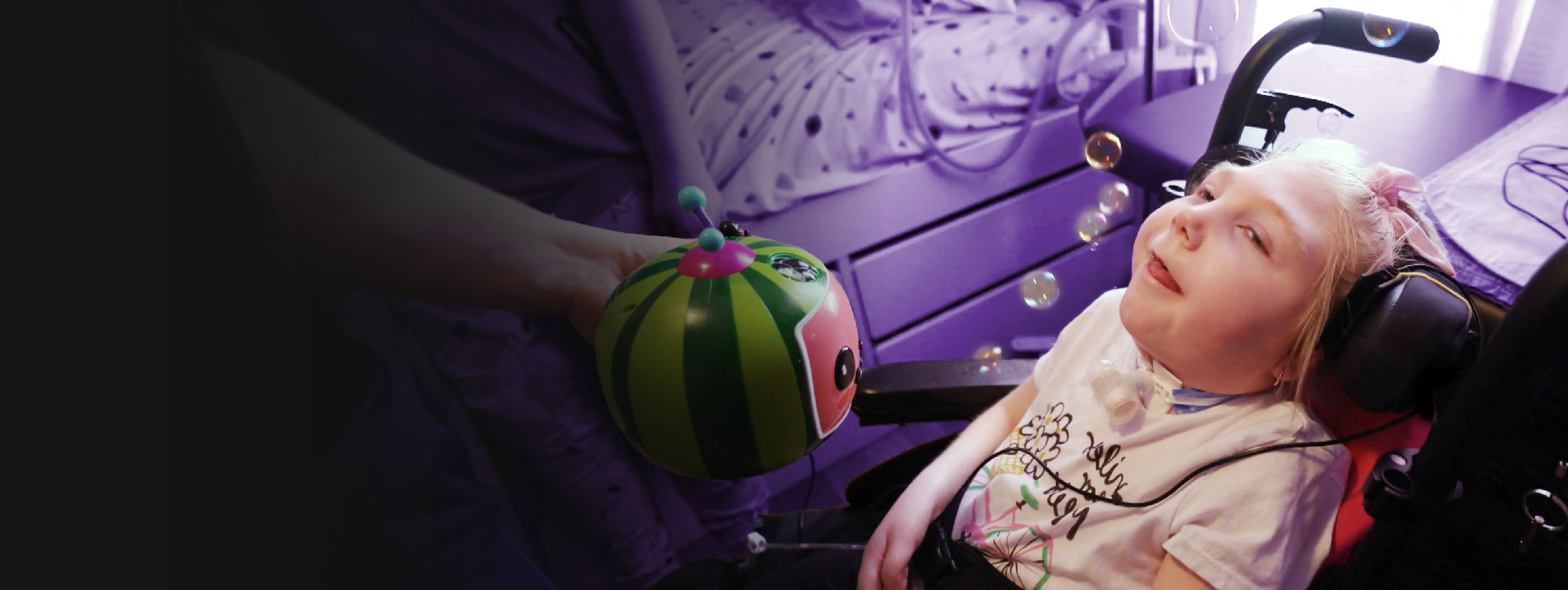 A young girl in a wheelchair looking at bubbles coming out of a coco melon bubble blower