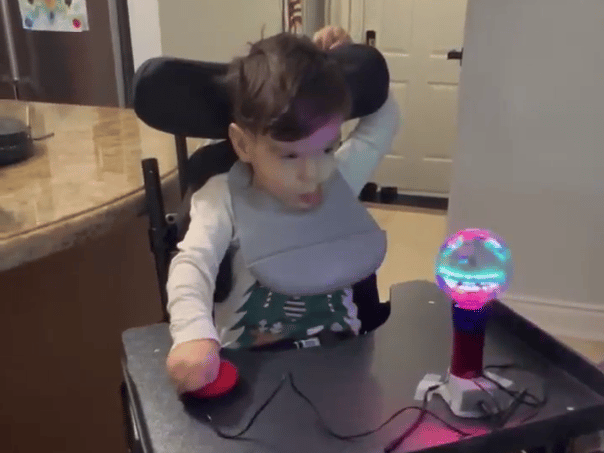 A young boy in a wheelchair pressing on a red switch connected to a spinning light wand