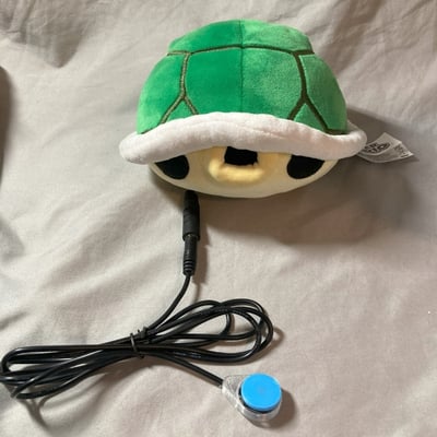 A raindrop switch plugged into a plush toy shaped as a Nintendo shell