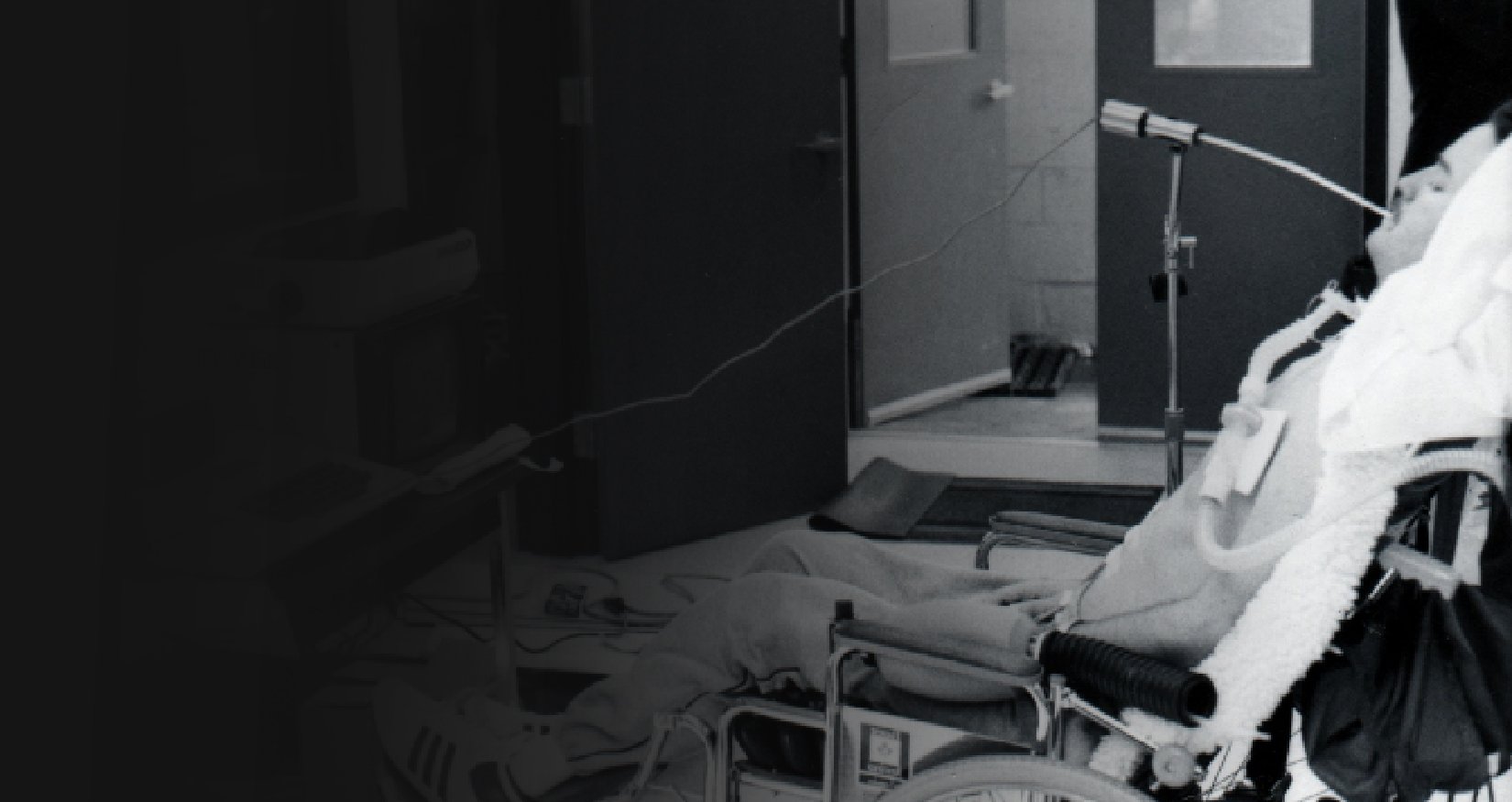 A black and white photo of Neil Squire in a wheelchair using a sip-and-puff device to type Morse Code.