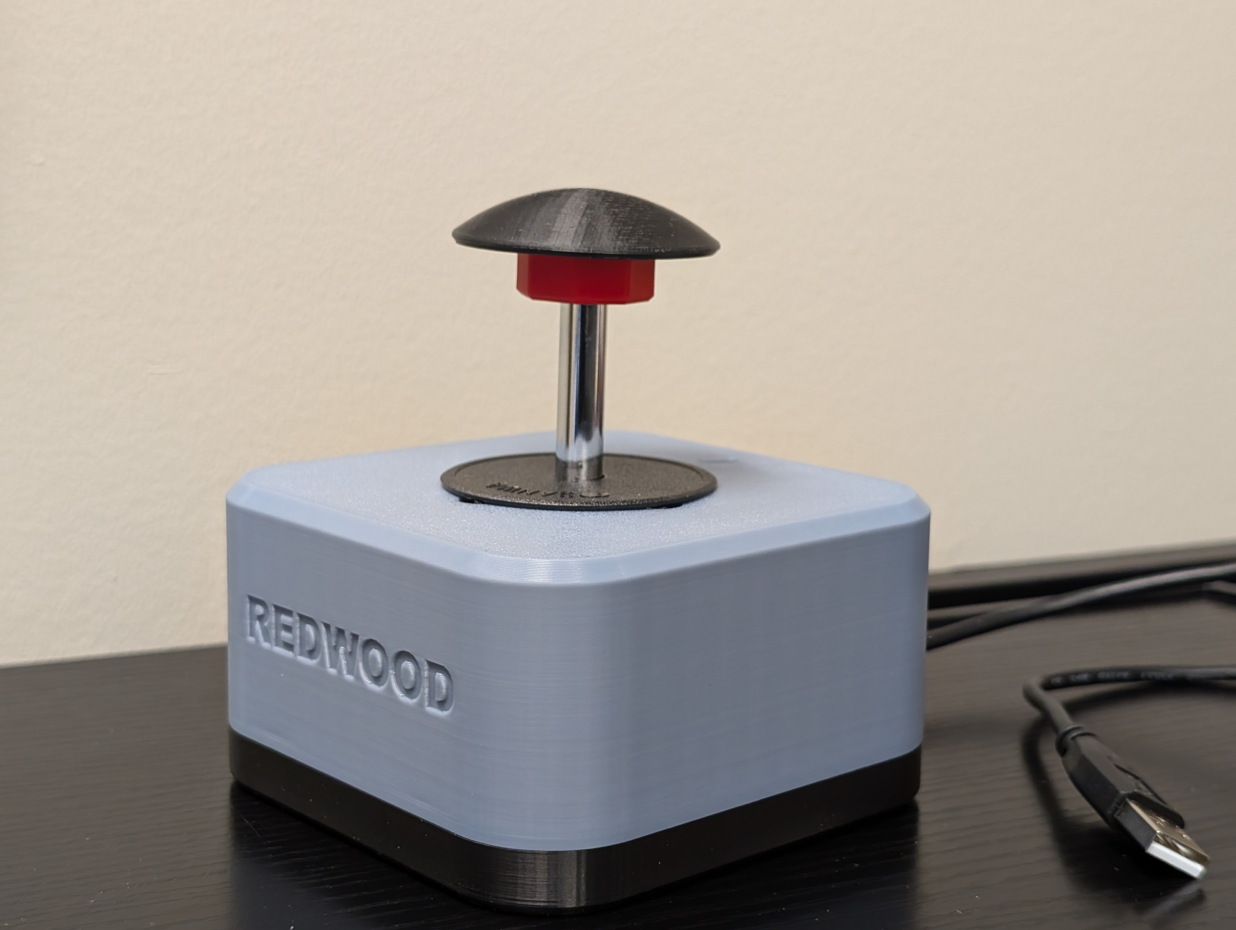 Isometric view of the Redwood joystick with a black 3D printed dome topper. A USB type A cable can be seen on the side. Top enclosure is light blue and base is black.