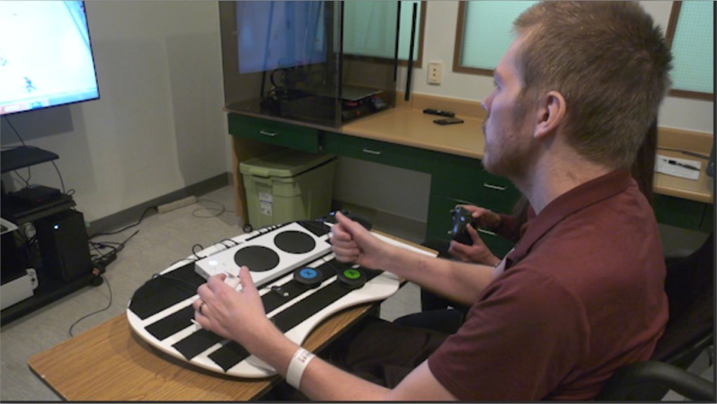 A man in a wheelchair using the Xbox Adaptive Controller and assistive switches to play video games.