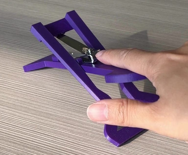 A hand pressing on a purple 3d printed nail clipper.