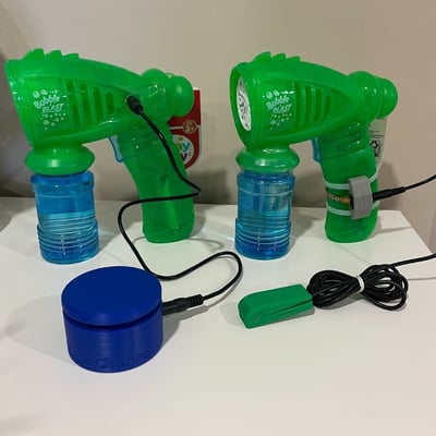 Two bubble blaster toys with assistive switches. The first toy has a MMC60 switch plugged directly into the toy. The second toy has a light touch switch plugged into a 3D printed jack holder.