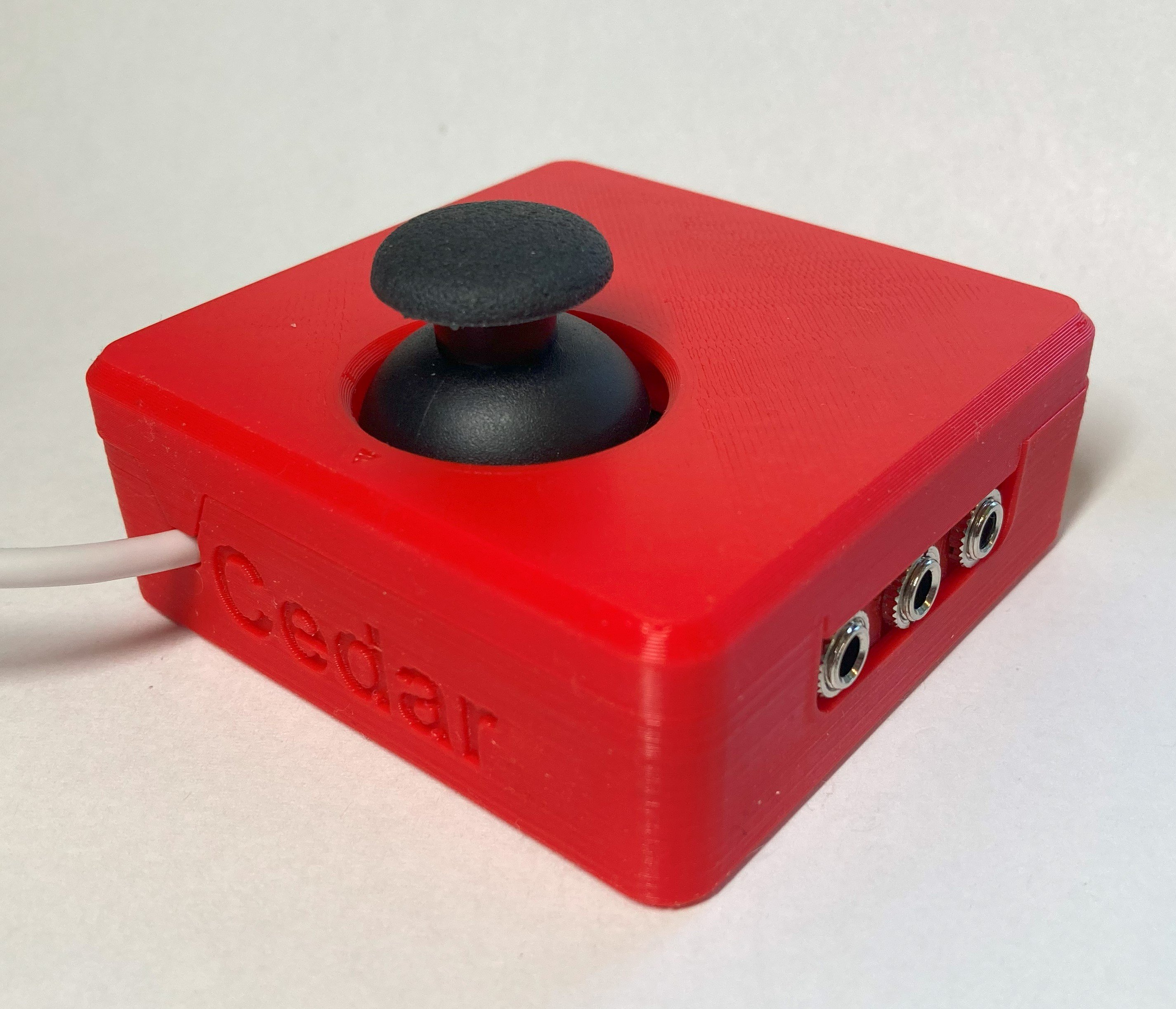 Small joystick with a red enclosure. Back view showing cable exit and 3 assistive switch ports.