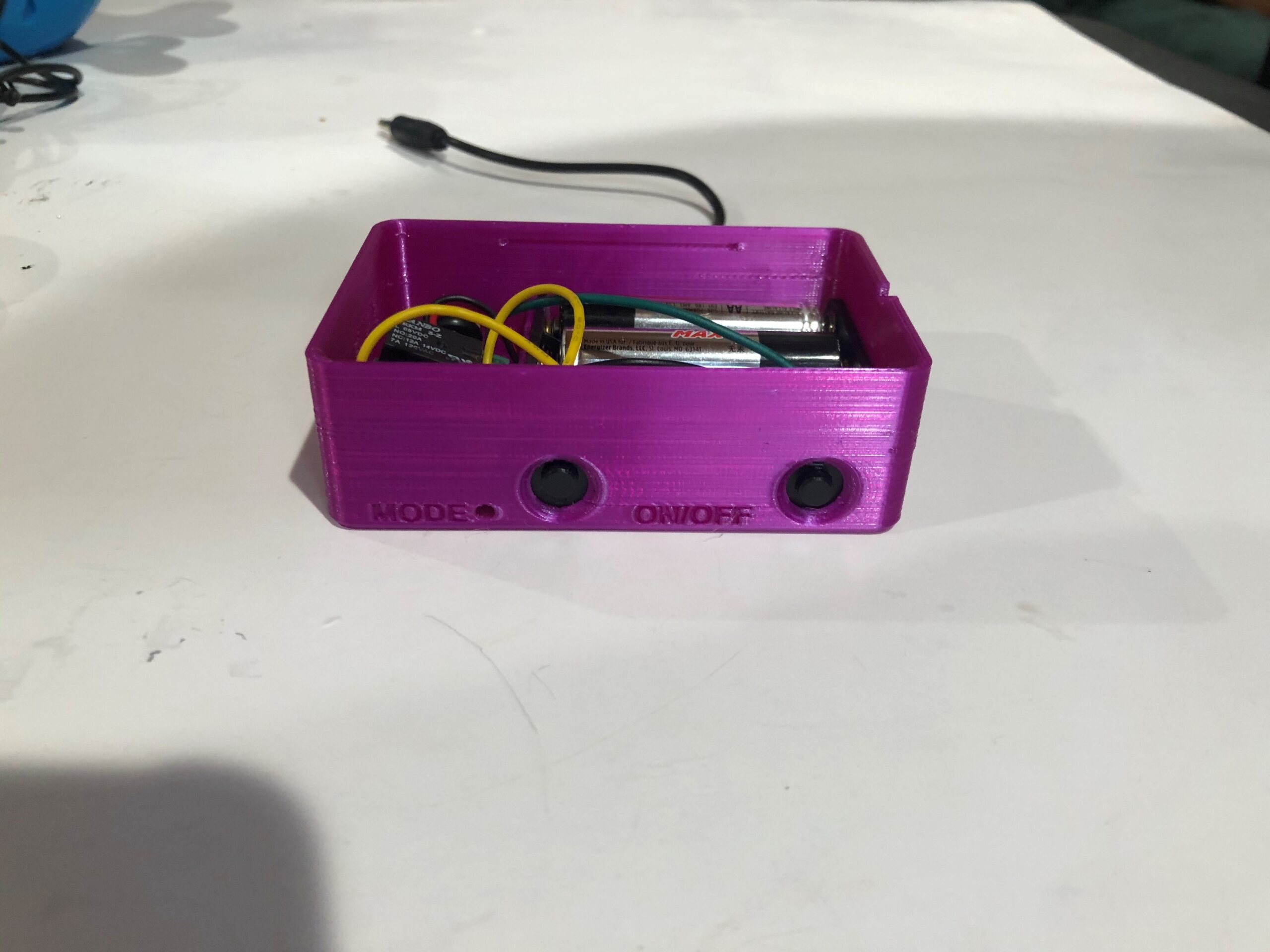 An uncovered pink wireless assistive switch link with wires inside and a black cable running out from the back.