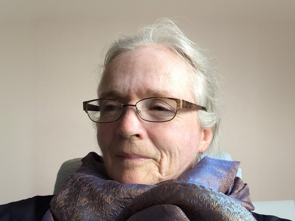 A women with white hair, gold glasses, and purple scarf.