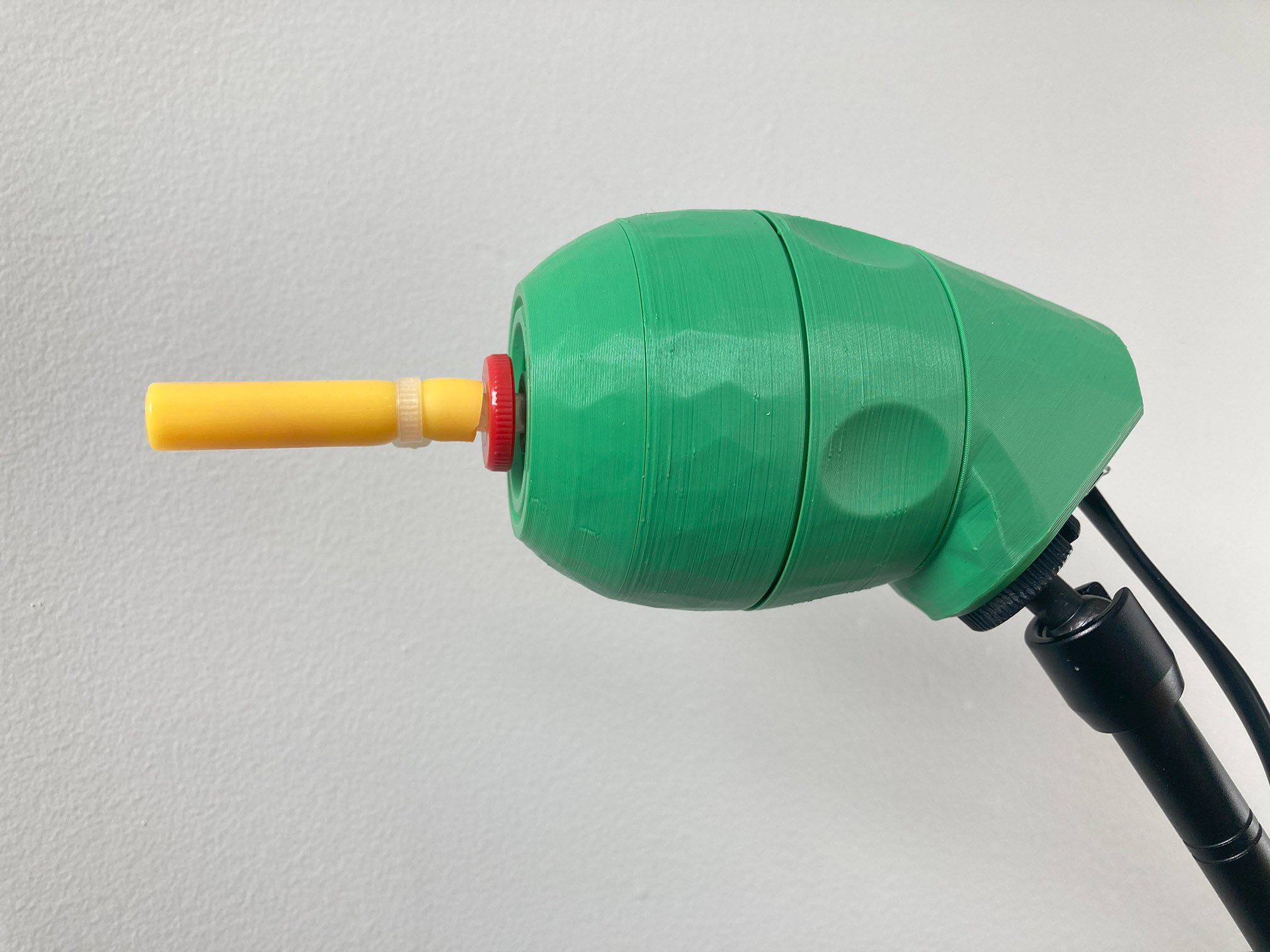 A green 3D printed LipSync joystick with a yellow mouthpiece