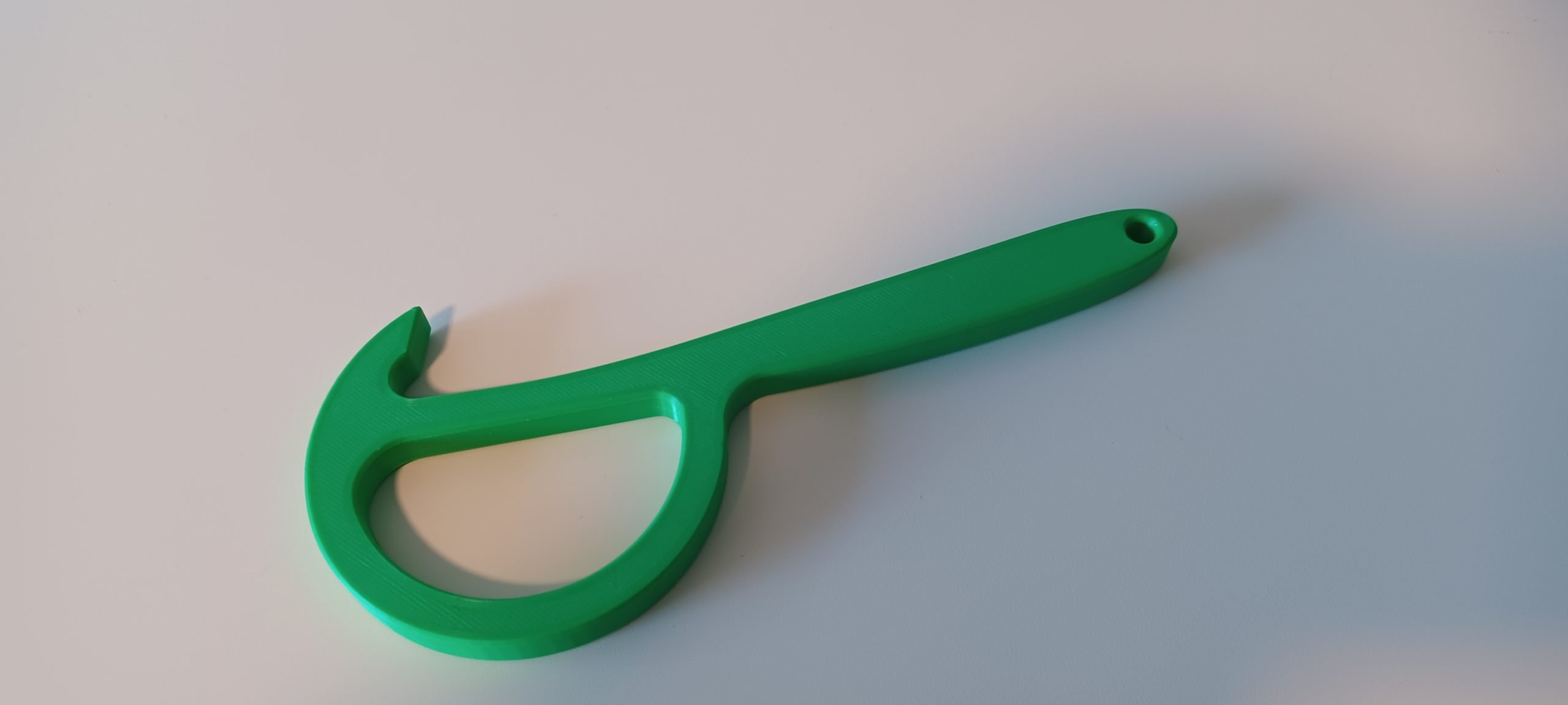 A green 3d printed pull tab opener on a white table.