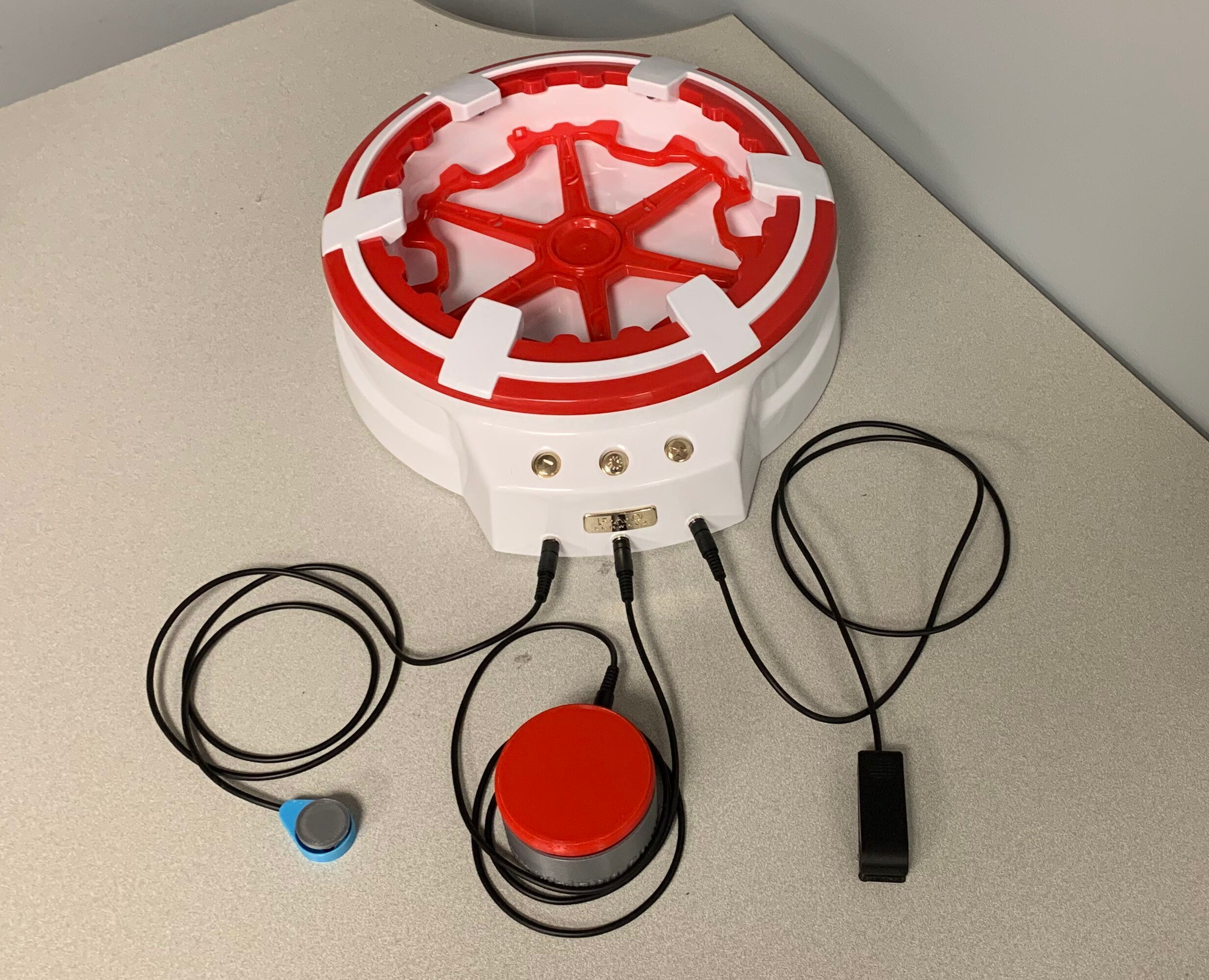 A red and white switch adapted spin art toy with three 3d printed assistive switches plugged in.