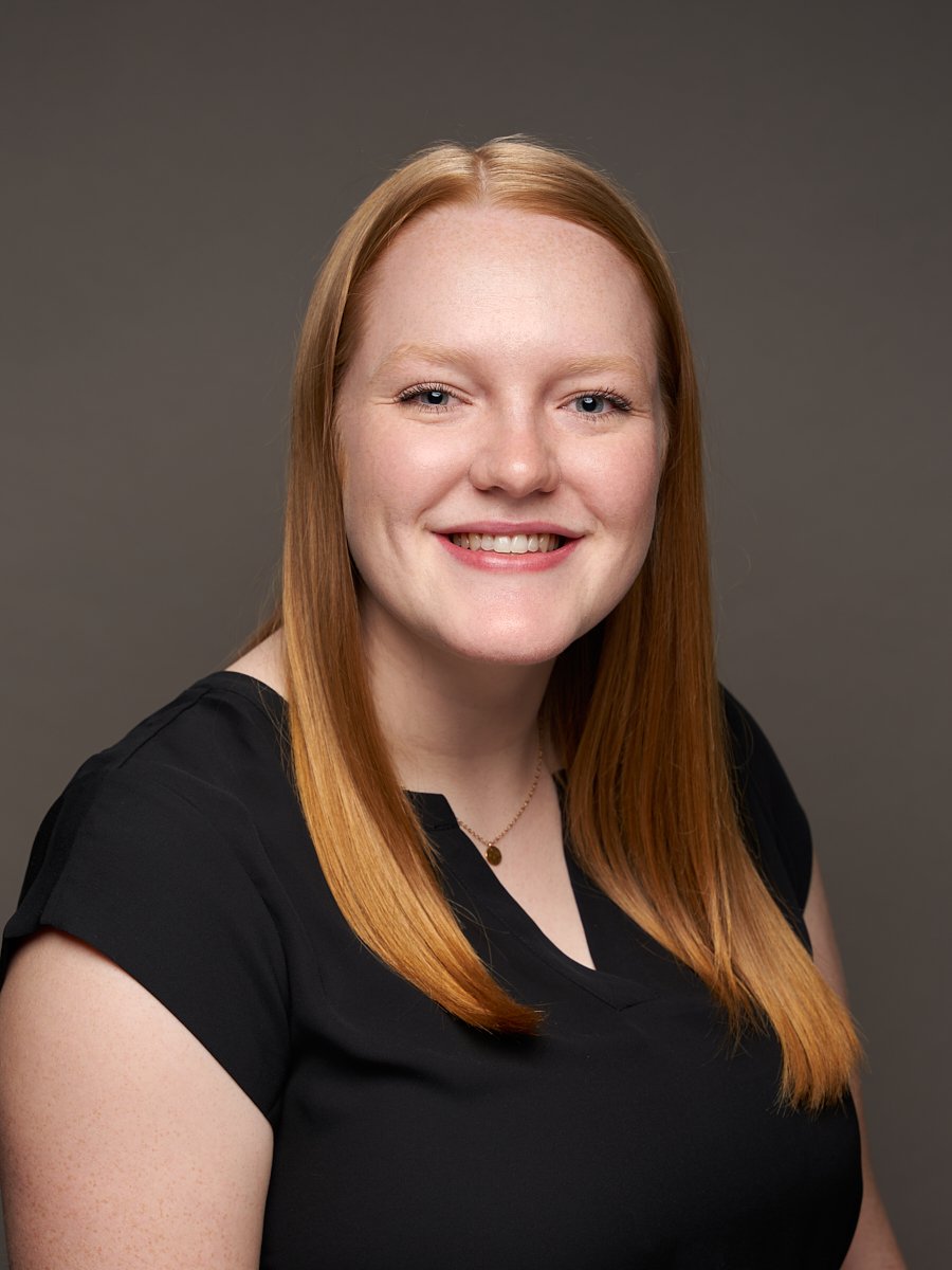 A woman with red straight hair and black blouse against a grey background.