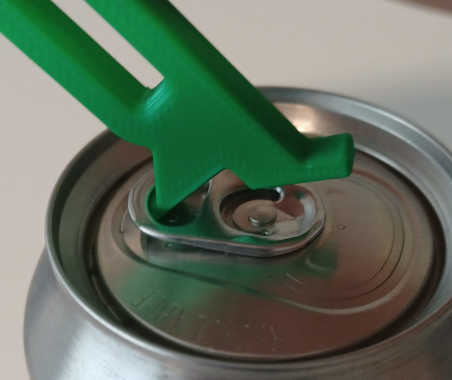 A green 3d printed beverage can opener hooked into a metal pull tab.