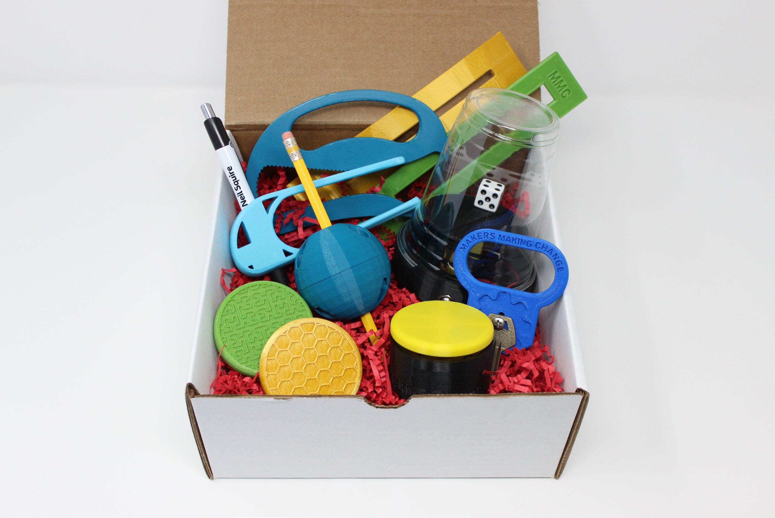 A box with 3d printed assistive devices like dyslexia reading bar, bottle opener, writing aids, dice spinner, key turner, and access switch