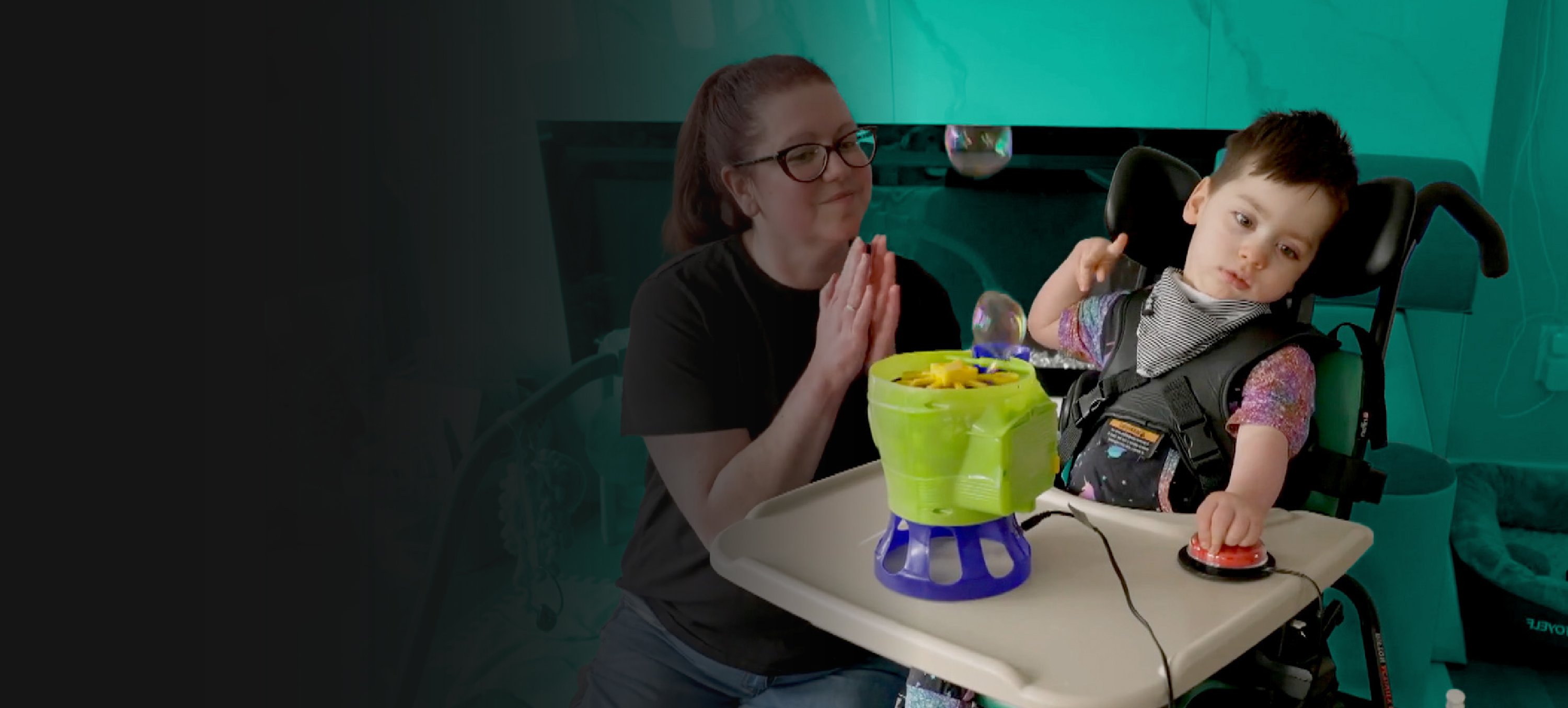 A young boy in a wheelchair operating a bubble blower using an assistive switch