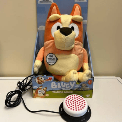 Orange Bingo plush toy in its box with a switch plugged in