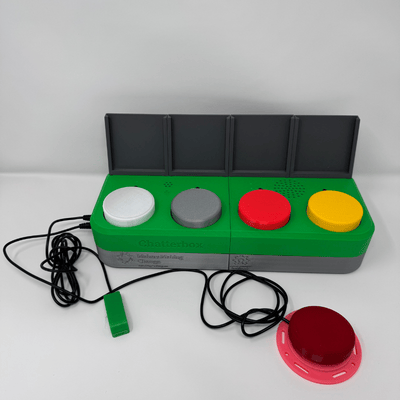 The Chatterbox with an Interact and Light Touch Assistive Switch connected to it. The Chatterbox is a wide, green rectangle with four circular buttons of different colours, and four grey squares on top.