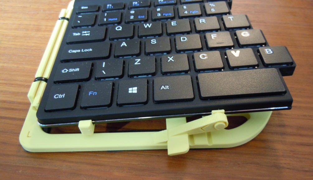 A yellow 3d printed tenting stand holding one half of a split keyboard at 5 degrees.