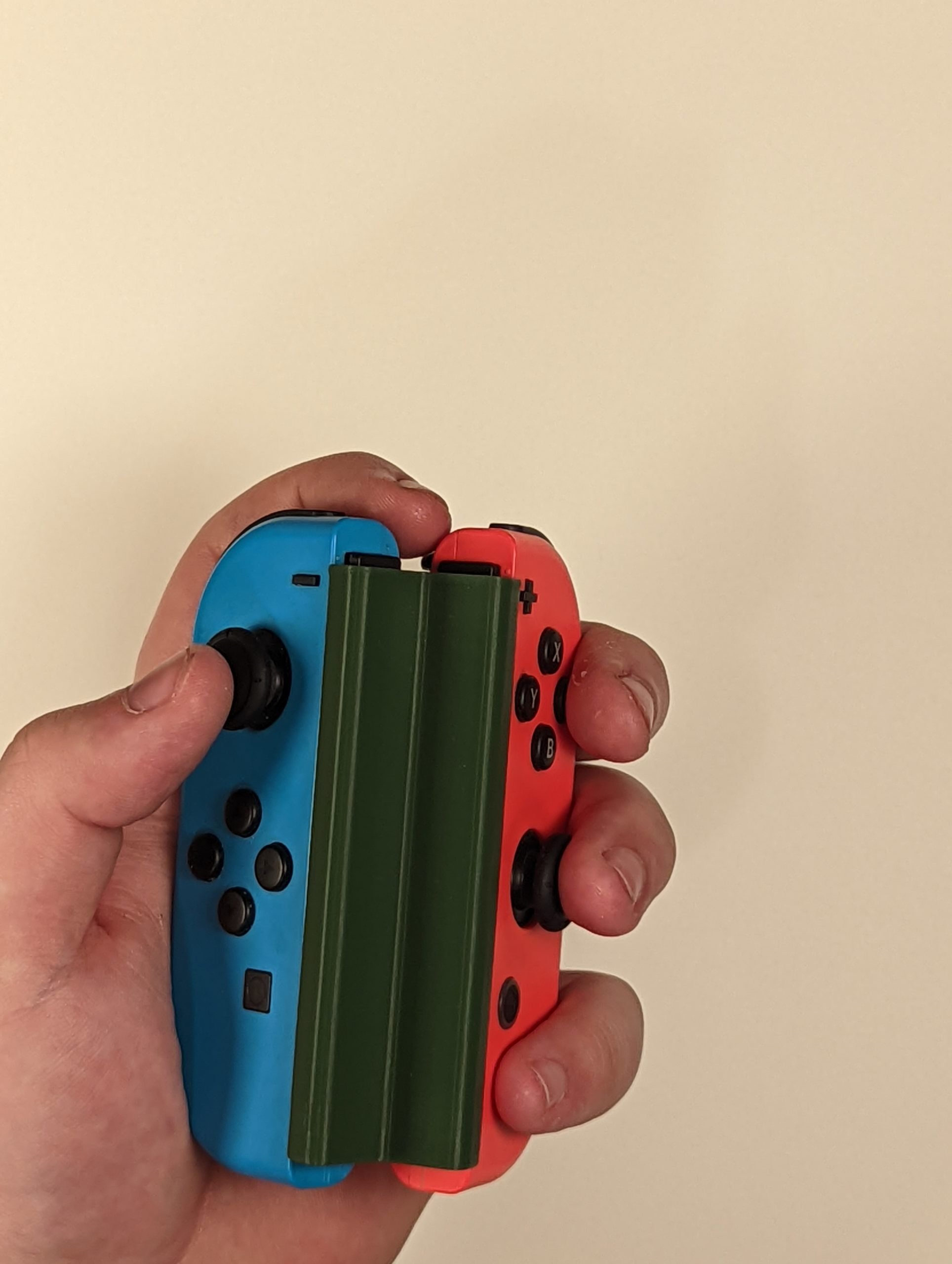Left hand holding blue and red joy-cons connected together by a green 3d printed adapter.