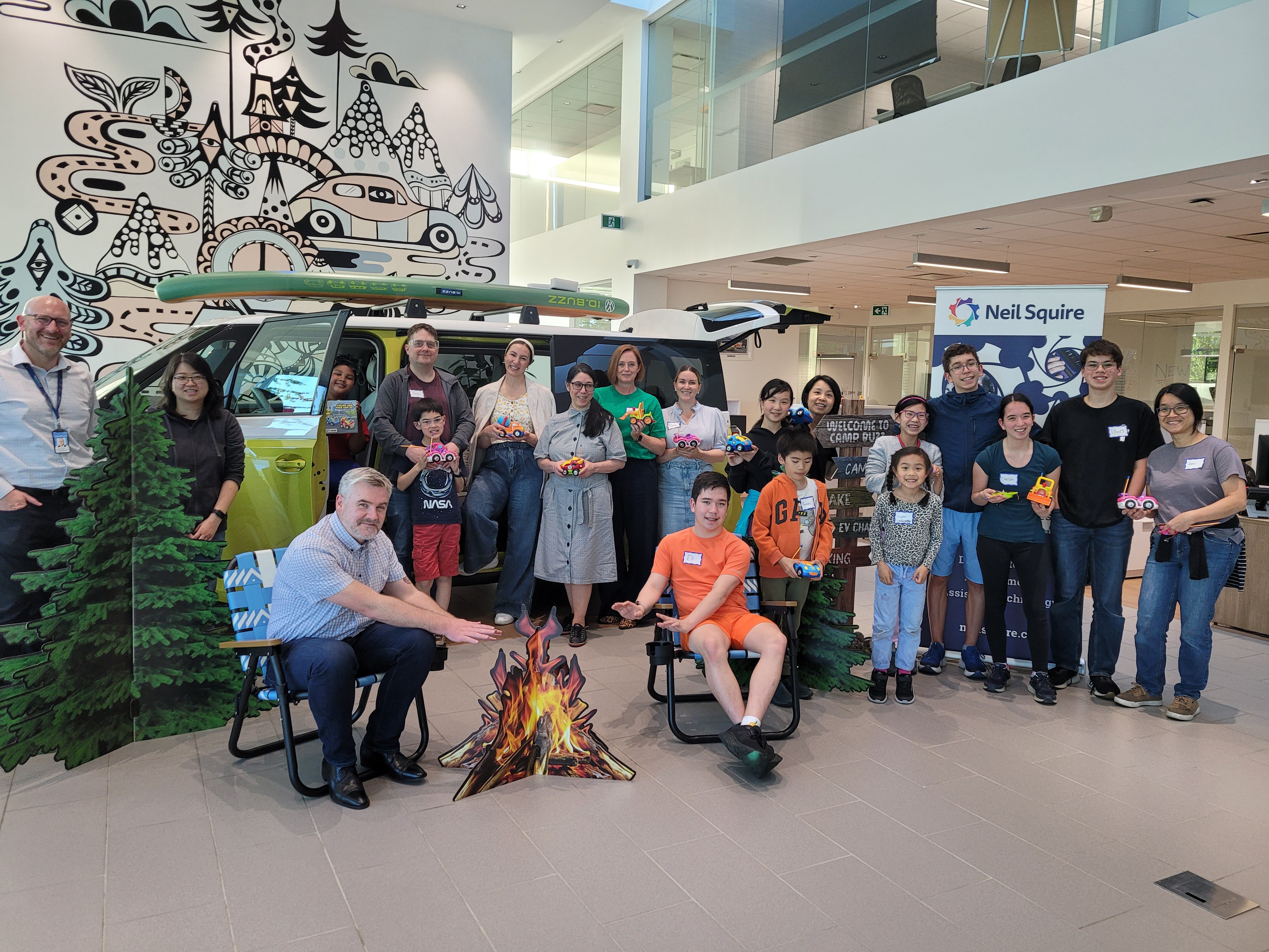 Staff and volunteers at OpenRoad Volkswagen Burnaby pose for a group photo, with a couple of members sitting around a pretend campfire.