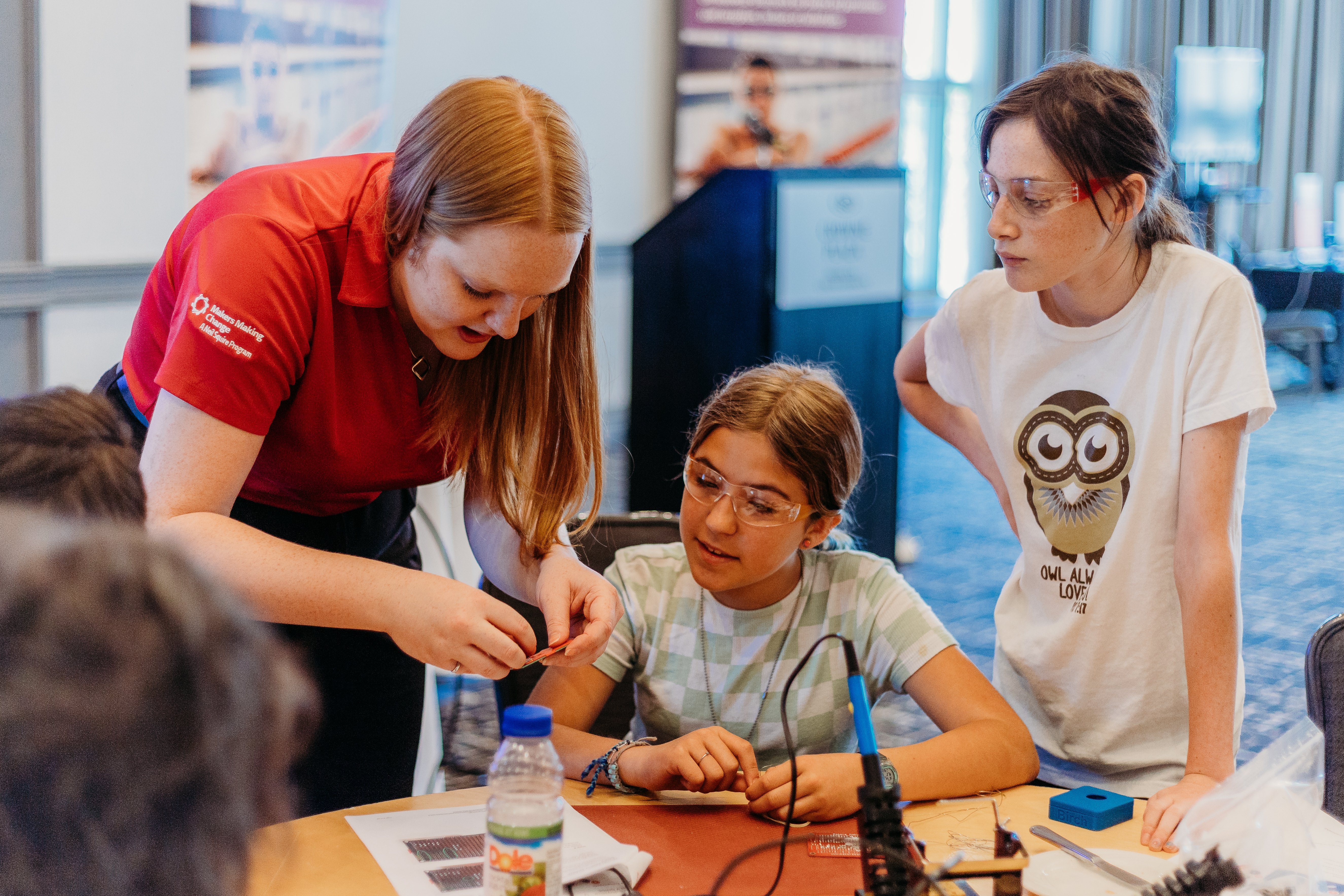 Two youth volunteers watching a staff person demonstrate device assembly.