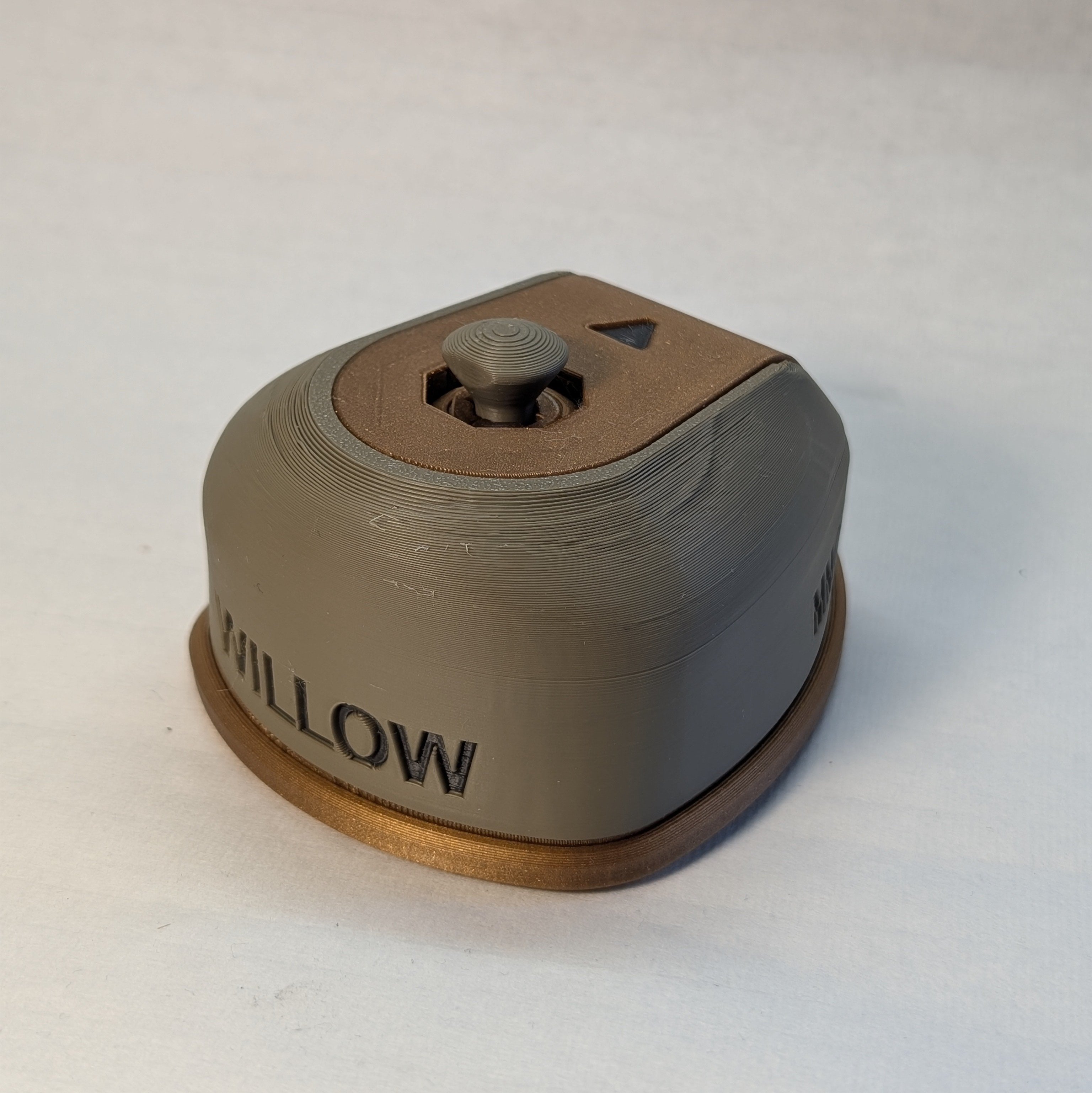 A front view of the Willow Joystick showing the name and orientation arrow. The joystick base is printed in gold and the shell in green. The joystick is using the convex topper.