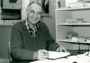 Black and White photo of Bill Cameron at a desk smiling