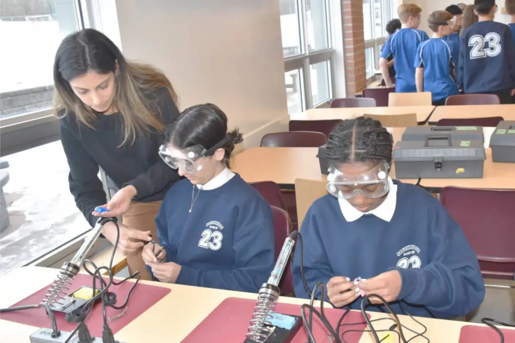 Two students and a teacher soldering at a table