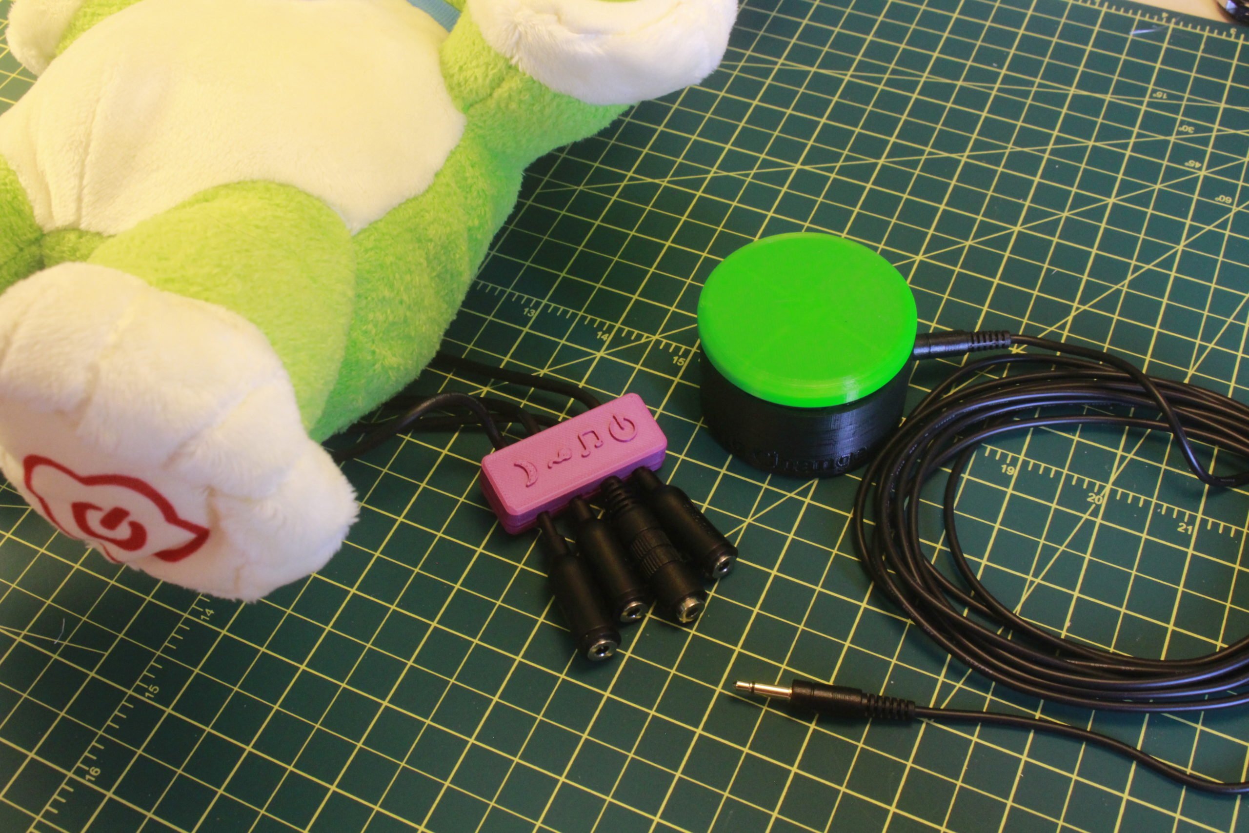 A purple 3d printed case holding four mono jacks from an adapted toy dog and a green assistive switch beside it.