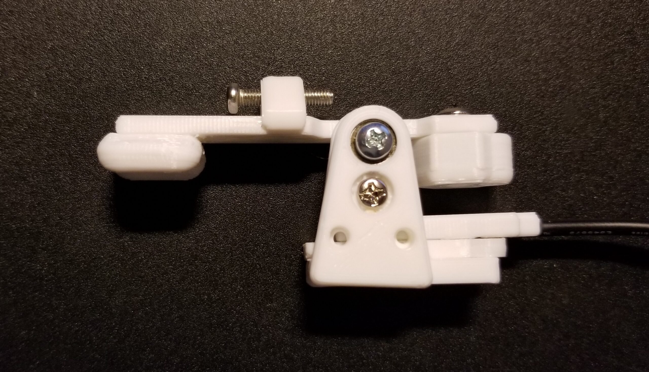 A white 3d printed finger lift switch on its side showing three metal screws and a black cord.