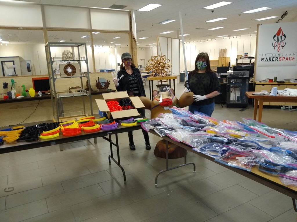 Two volunteers and two tables containing parts for assistive devices.