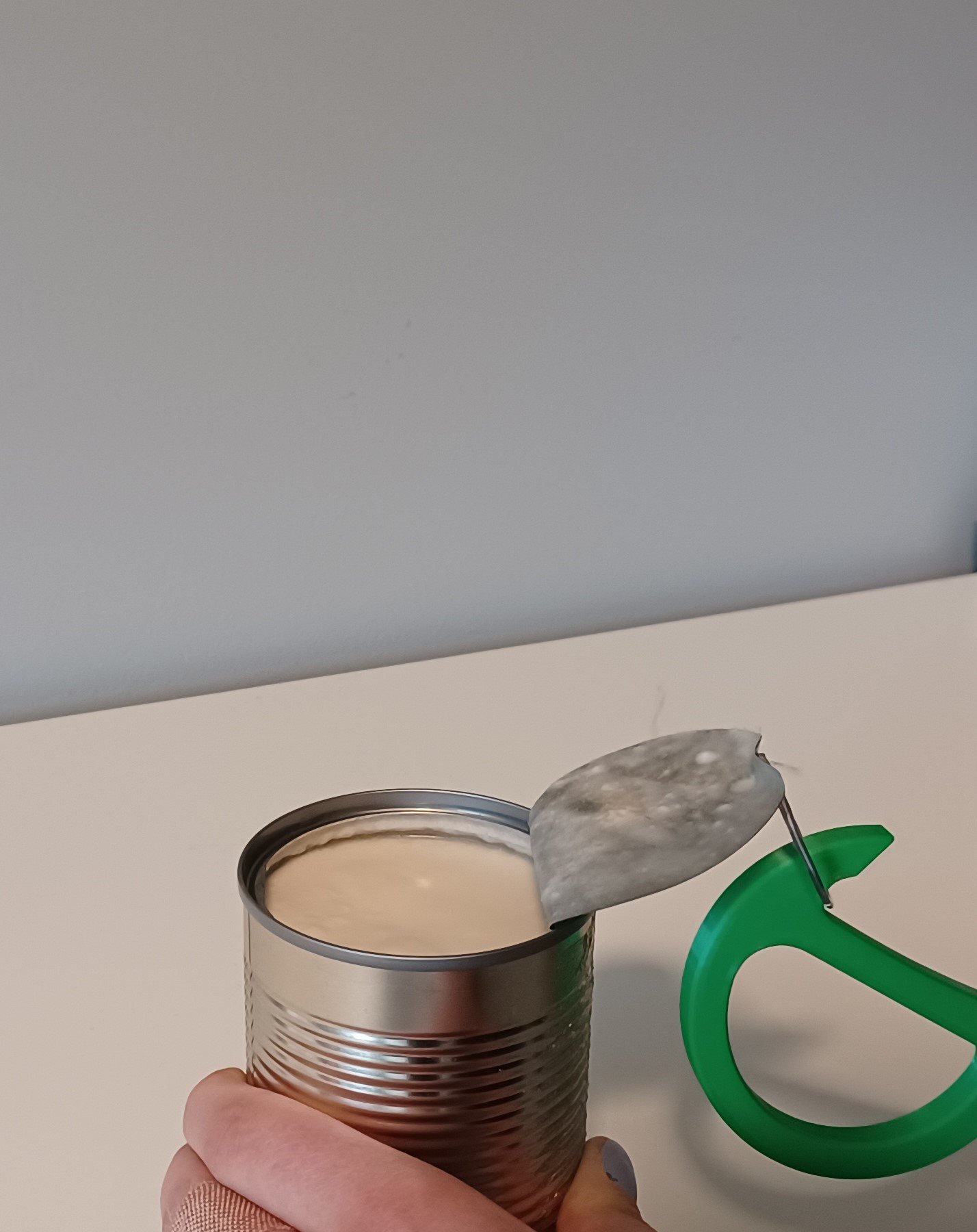 An opened tin can with a green 3D printed can opener hooked on the metal pull tab.