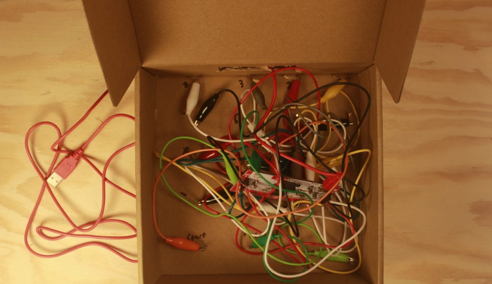 An uncovered cardboard box with tangled alligator clips inside.