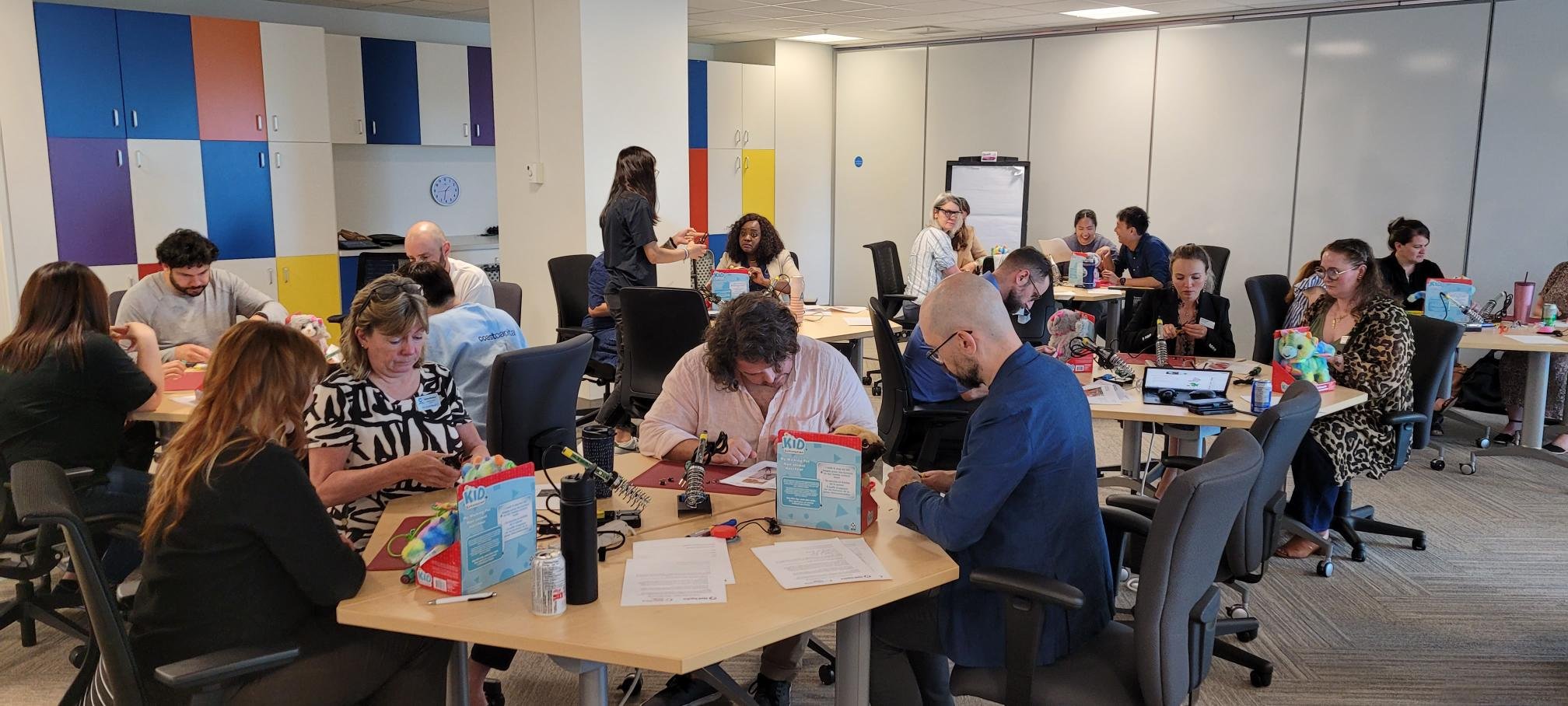 A group of workers adapting toys with various tools in a colorful boardroom
