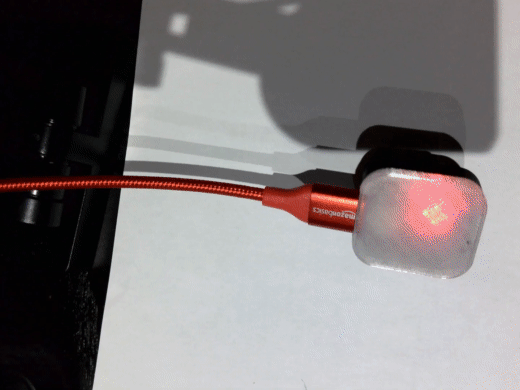 A 3d printed translucent device with red, blue, and green light shining through. A red USB cable is plugged into the device.