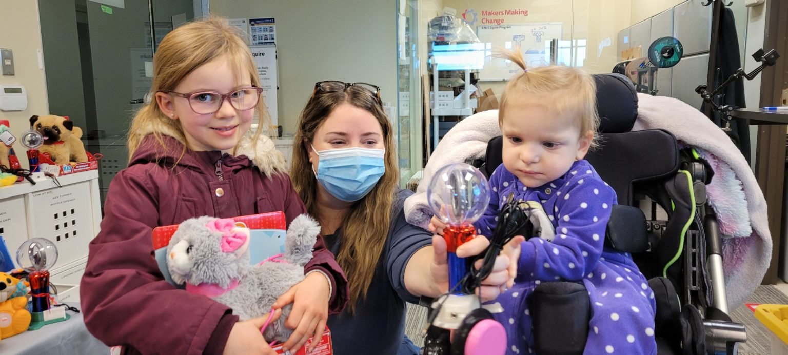 Two kids and their guardian holding switch-adapted toys.