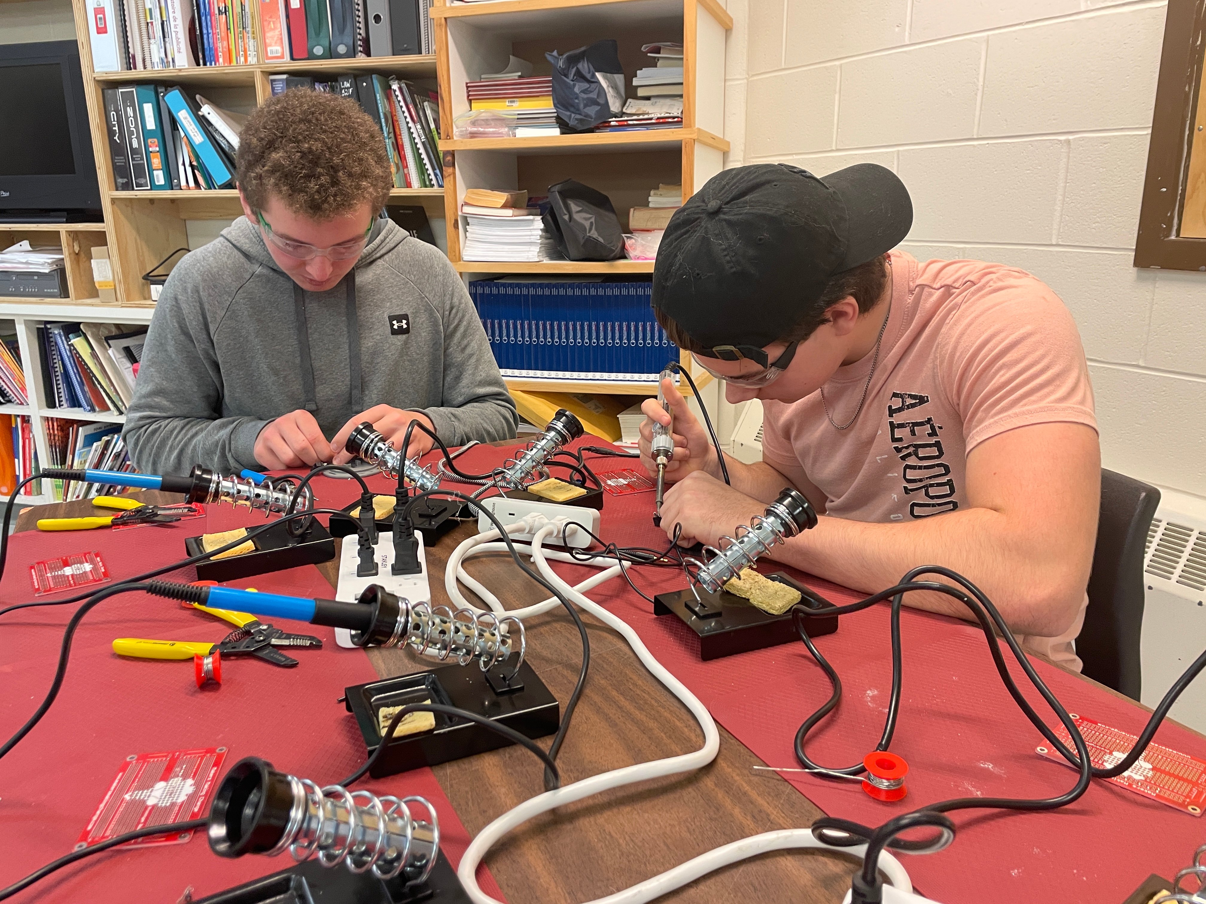 Two youth makers soldering at a table with various hand tools and soldering irons