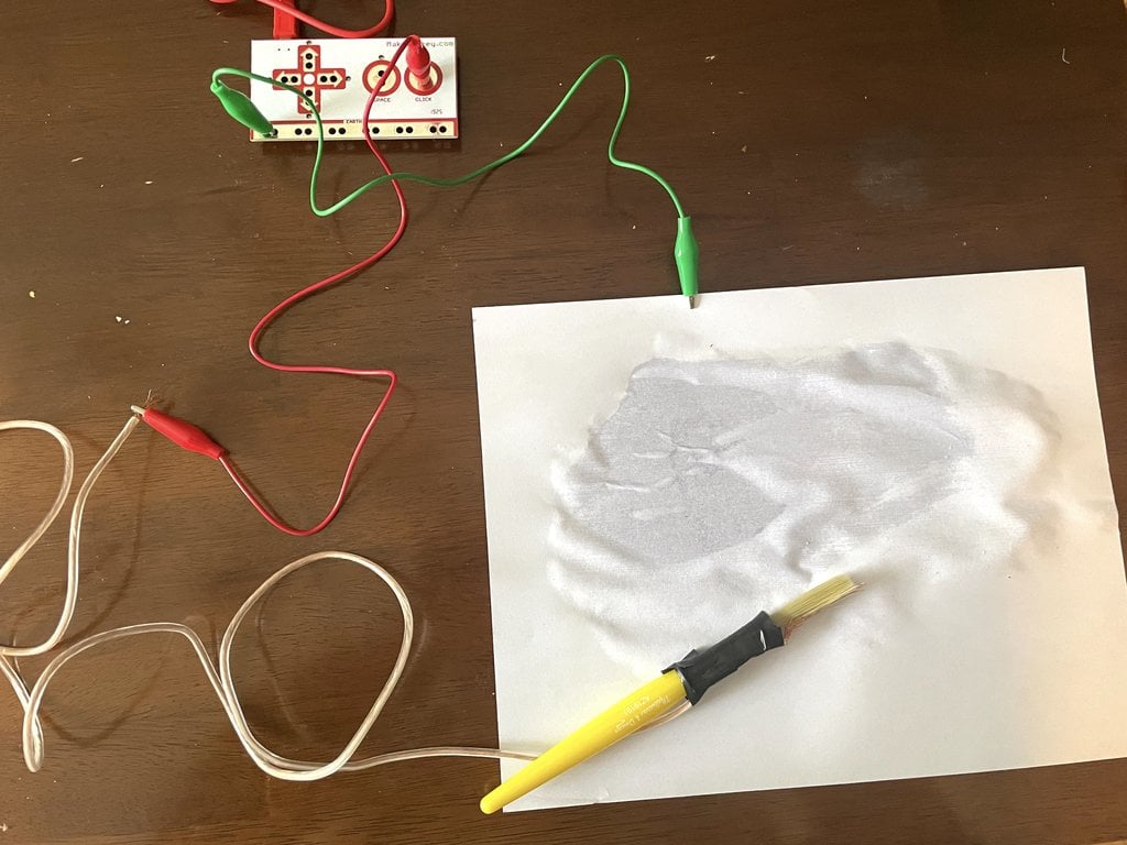 Paint brush attached to Makey Makey resting on wet paper
