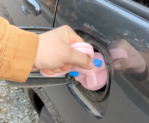 A hand holding our pink Gas Cap Opener.