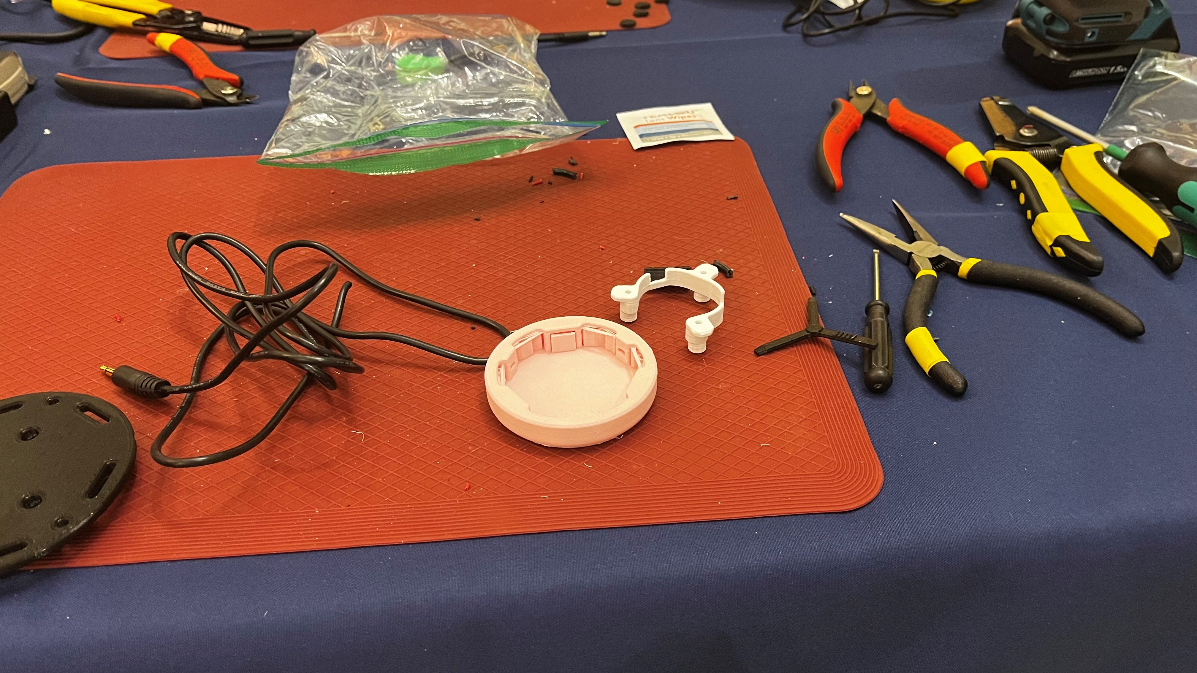 A soldering workstation with a 3D printed part, a cable, plyers, and various tools.