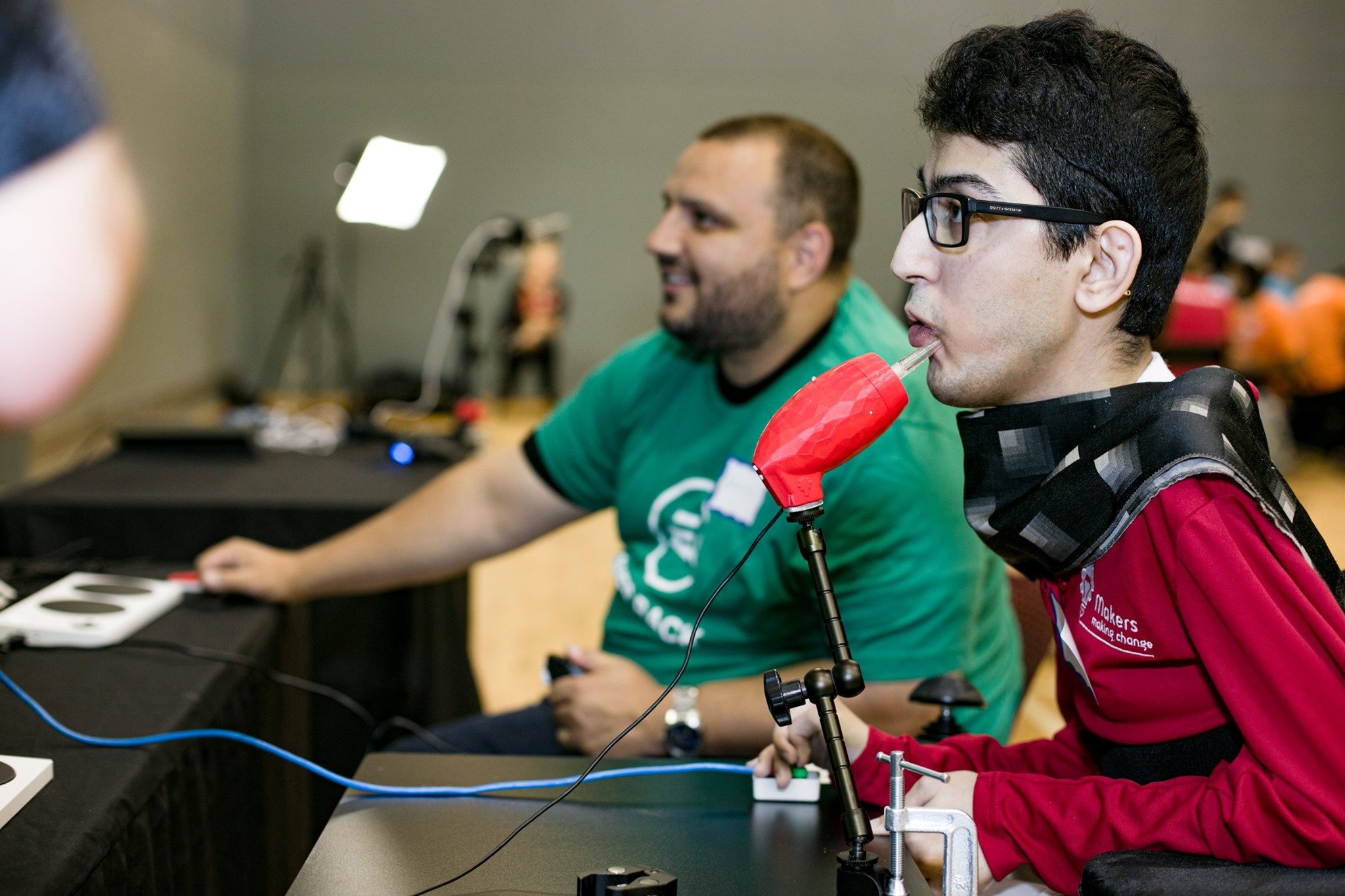 Milad uses a LipSync device to gaming with a friend who is seated in the backgroun